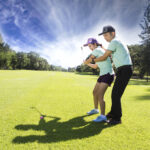 Young female golf player at Driving Range with a Golf Pro