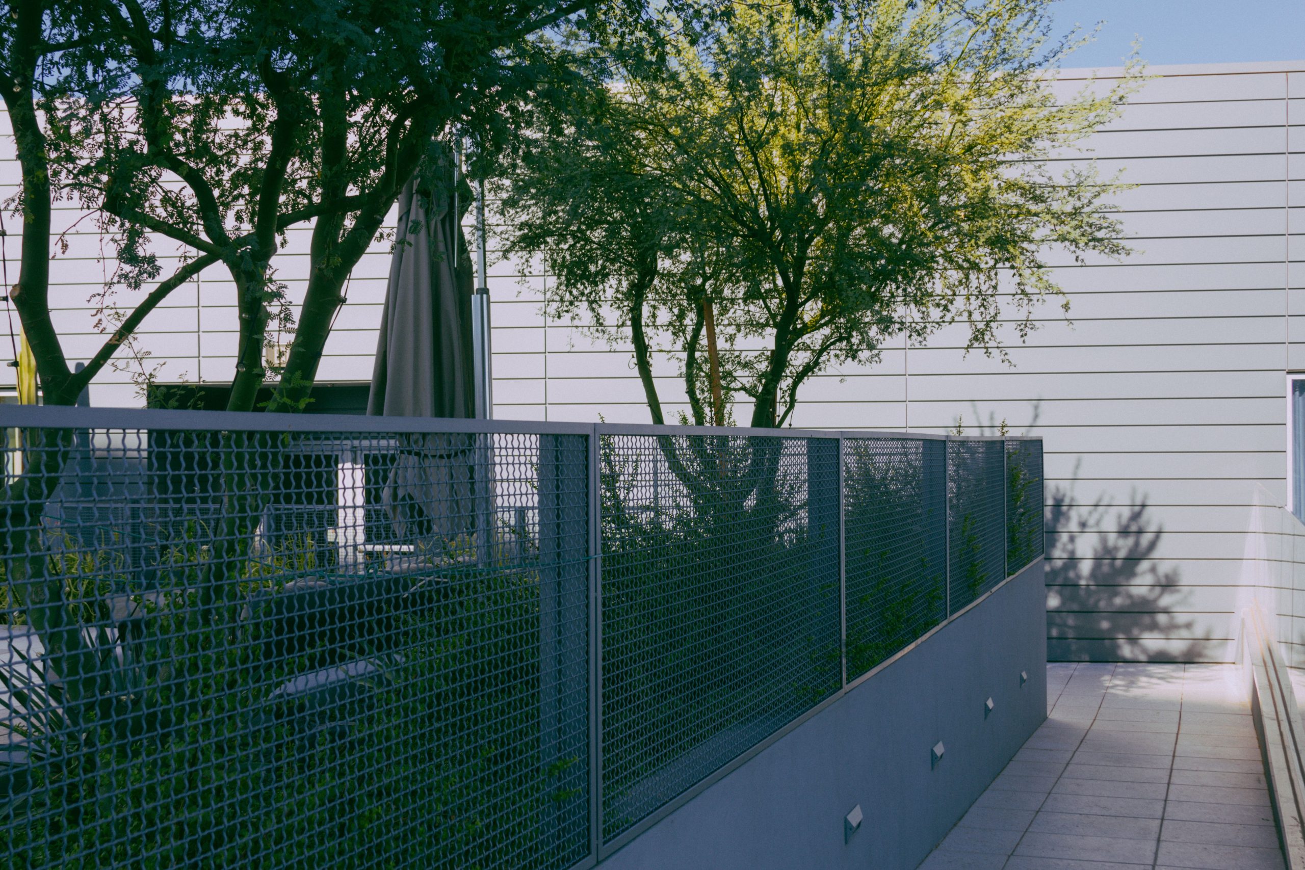 modern-metal-garden-fence-privacy Contemporary urban patio with a sleek metal fence, trees, and sunlight